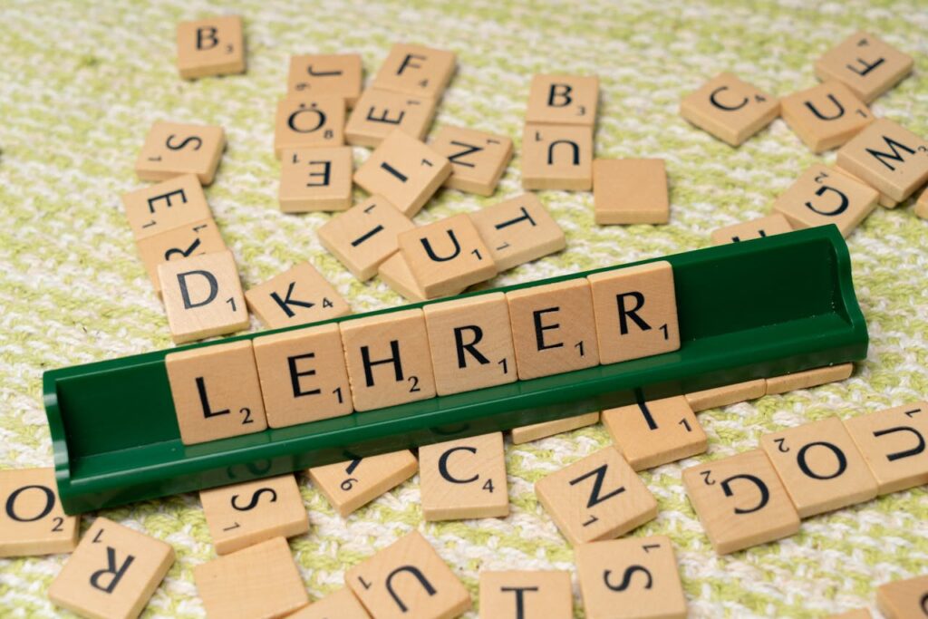 Wooden letter tiles spelling 'Lehrer' on a green rack, surrounded by scattered tiles.